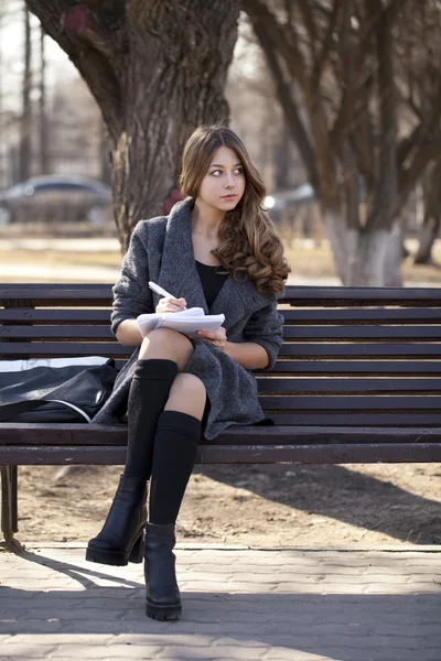 Estudante sentado em um banco com um caderno no parque da primavera — Fotografia de Stock