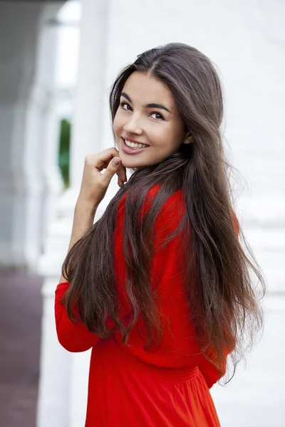 Gelukkig jonge vrouw in rode jurk tegen de achtergrond van een blok — Stockfoto