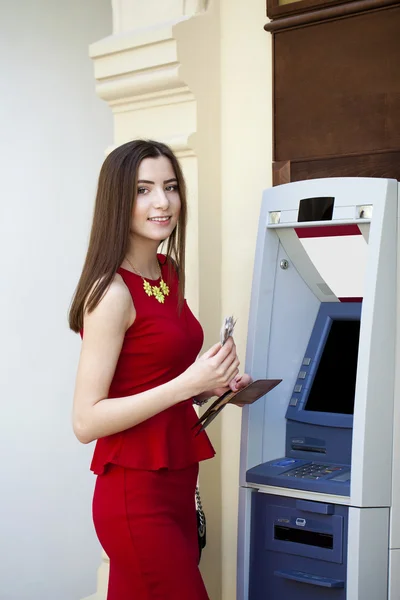 Giovane donna in abito rosso utilizzando un sportello automatico — Foto Stock