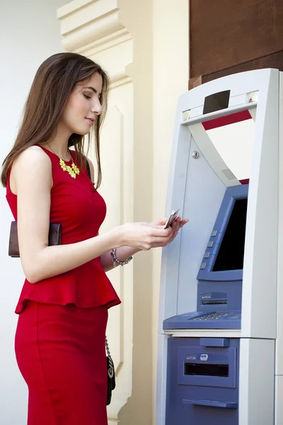 Młoda kobieta w czerwonej sukience za pomocą bankomat — Zdjęcie stockowe