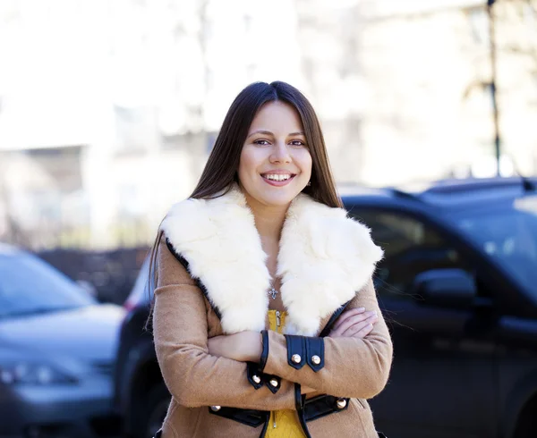 Glad ung flicka i FÅRSKINNSPÄLS på en bakgrund av staden — Stockfoto