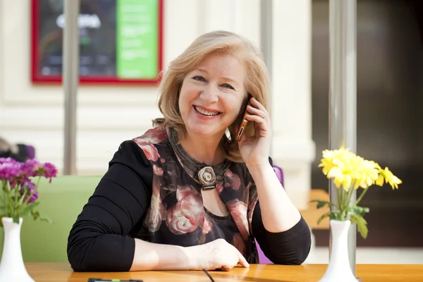 Mature beautiful woman is calling on a cell phone while sitting — Stock Photo, Image