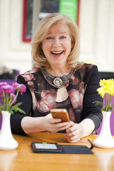 Mature blonde woman reads the message on the phone while sitting — Stock Photo, Image