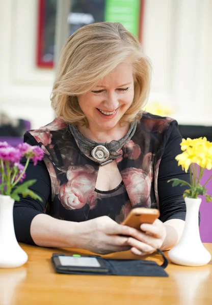 Зріла блондинка читає повідомлення по телефону, сидячи — стокове фото