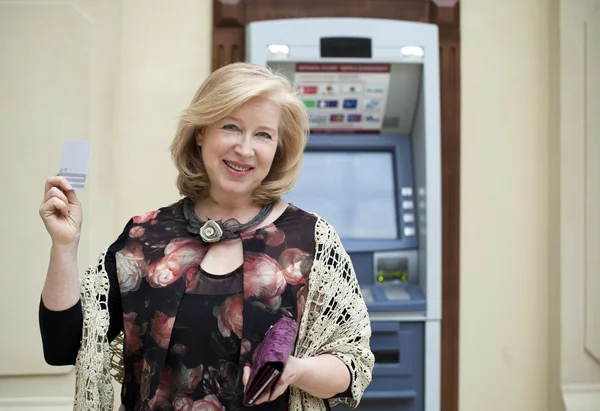 Зрелая блондинка с кредиткой в руке возле банкомата — стоковое фото