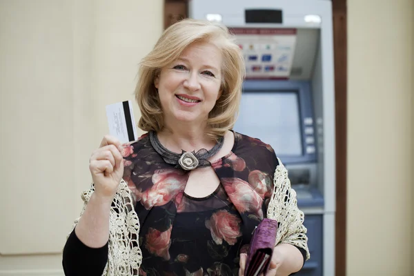 Зрелая блондинка с кредиткой в руке возле банкомата — стоковое фото