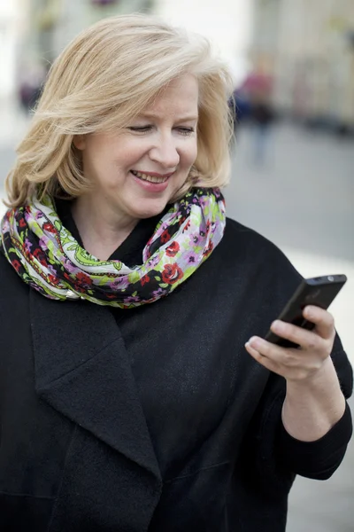 Mature blonde woman reads the message on the phone — Stock Photo, Image