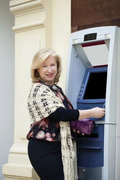 Mature blonde woman with credit card in hand near ATM — Stock Photo, Image