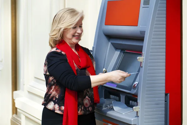 Зріла блондинка з кредитною карткою в руці біля банкомату — стокове фото