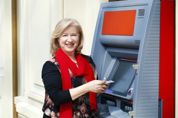 Mature blonde woman with credit card in hand near ATM — Stock Photo, Image