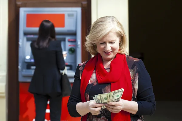Зрелая блондинка считает деньги возле банкомата — стоковое фото