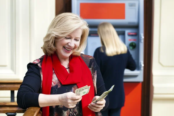 Mature blonde woman counting money near ATM — Stock Photo, Image