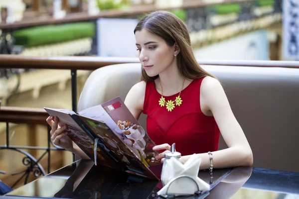 Menina bonita sentada em um café e considera o menu — Fotografia de Stock