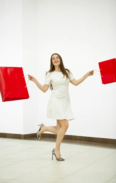Wanita bahagia memegang dua tas belanja merah berjalan di toko — Stok Foto