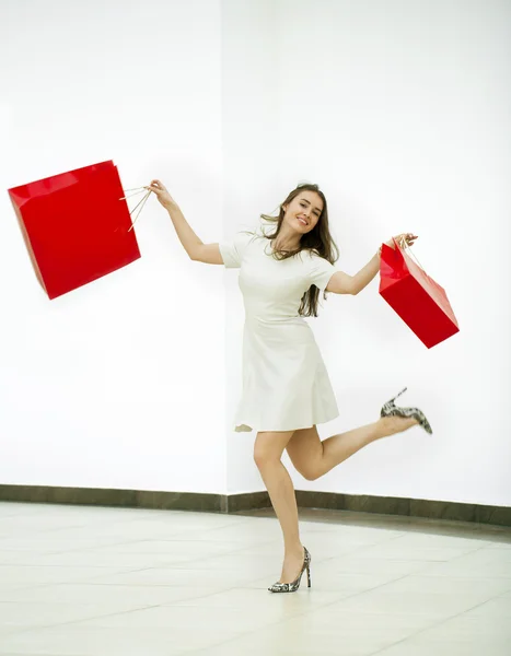 Happy woman holding two red shopping bags walking in the shop — Stock Photo, Image