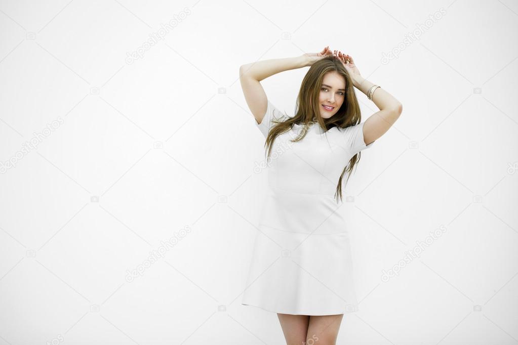 Beautiful young woman in a light gray dress posing against a whi