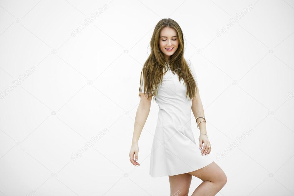Beautiful young woman in a light gray dress posing against a whi