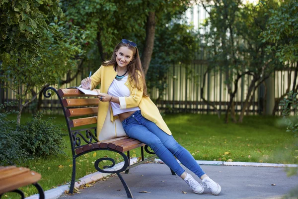 Happy young brunette sitting on a park bench — Stock Photo, Image