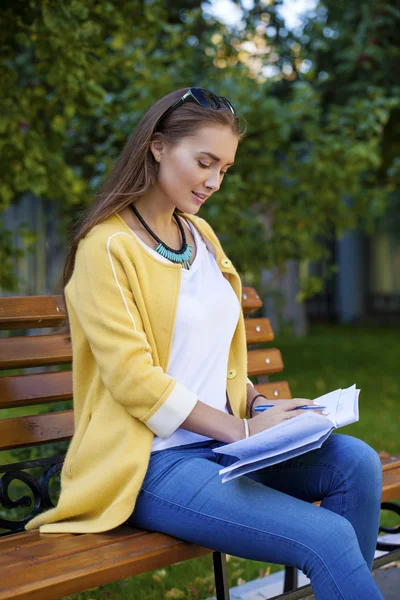 Szczęśliwa młoda brunetka, siedząc na ławce w parku — Zdjęcie stockowe