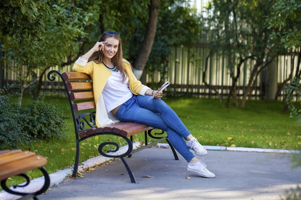 Счастливая юная брюнетка сидит на скамейке в парке — стоковое фото