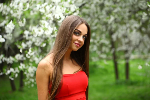 Happy young woman in red dress against the background spring flo — Stock Photo, Image