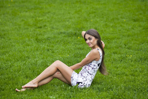 Mulher sexy em vestido curto sentado na grama verde — Fotografia de Stock