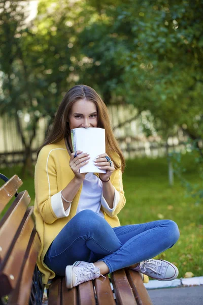 Joyeux jeune brunette assise sur un banc de parc — Photo