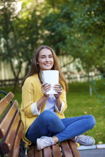 Jovem morena feliz sentada em um banco de parque — Fotografia de Stock