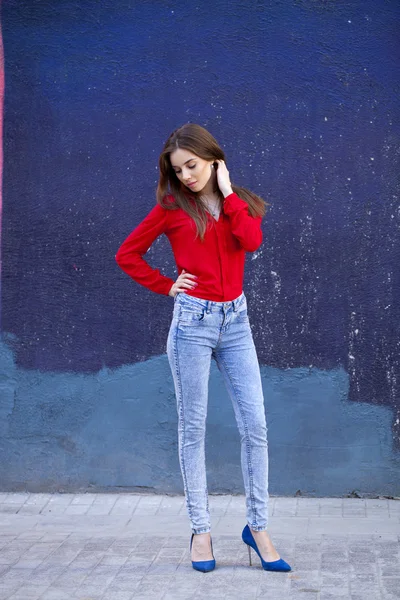 Joven chica hermosa en vaqueros azules y una camisa roja en el backgr — Foto de Stock