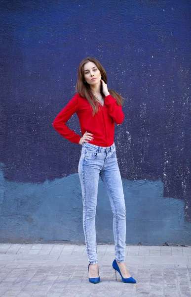 Young beautiful girl in blue jeans and a red shirt on the backgr — Stock Photo, Image