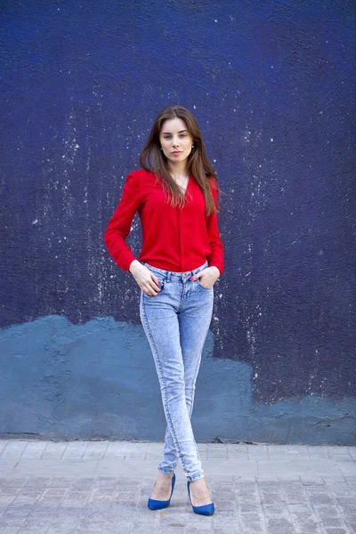 Ung vacker flicka i blå jeans och en röd tröja på bakgrunds — Stockfoto