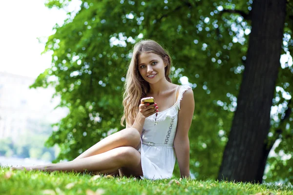 Glada vackra blonda tjejen ringer via telefon i en sommar park — Stockfoto