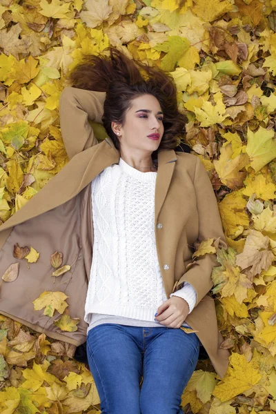 Young beautiful girl in blue jeans lying on yellow leaves — Stock Photo, Image