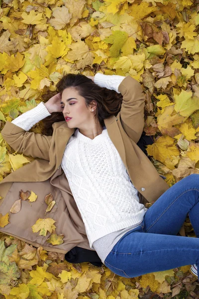 Jovem menina bonita em jeans azul deitado em folhas amarelas — Fotografia de Stock