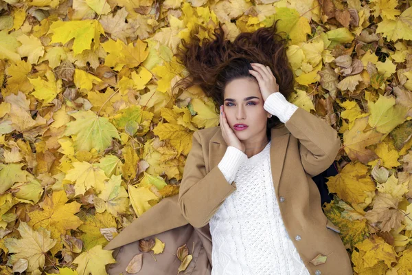 Young beautiful girl in blue jeans lying on yellow leaves — Stock Photo, Image