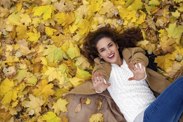 Jovem menina bonita em jeans azul deitado em folhas amarelas — Fotografia de Stock