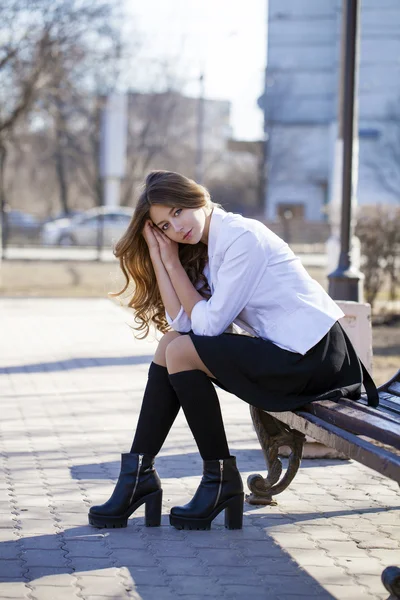 Jonge mooie blonde schoolmeisje zittend op een bankje — Stockfoto