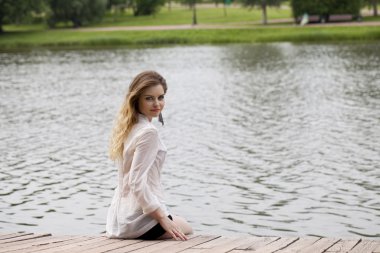 Genç kız güzel bir beyaz tunik t ahşap bir iskele oturur