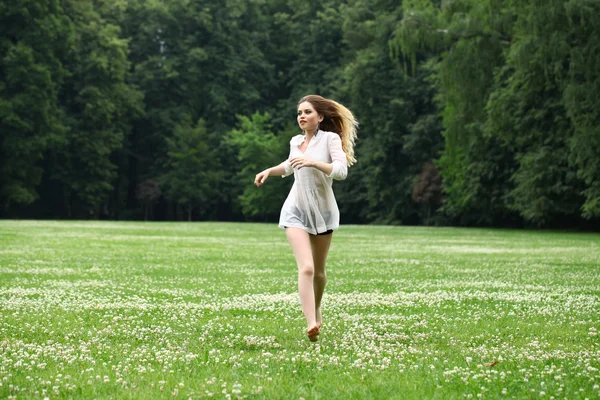 Young beautiful girl in the white shirt is running on the green — Stock Photo, Image