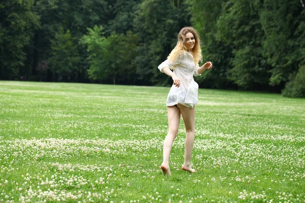 Jovem menina bonita na camisa branca está correndo no verde — Fotografia de Stock