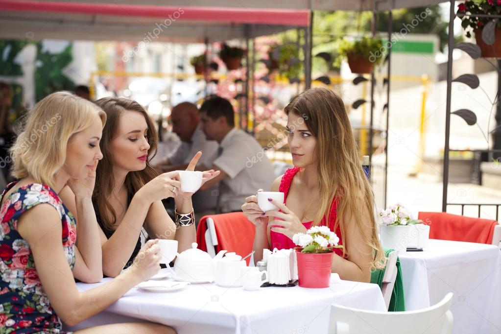 Three happy girlfriends woman sitting at a table in the summer c