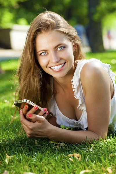 Happy beautiful blonde girl calling by phone in a summer park — Stock Photo, Image