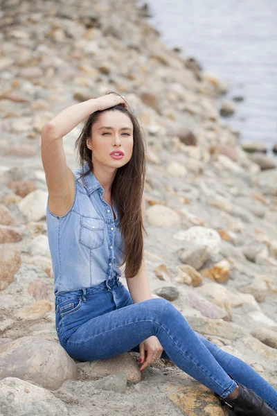 Young beautiful brunette girl sitting on the rocks on the river