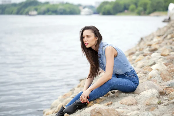 Junge schöne brünette Mädchen sitzt auf den Felsen auf dem Fluss — Stockfoto