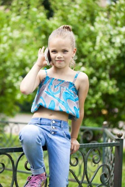 Kleines Mädchen telefoniert mit Handy gegen Grün des Parks in Summen — Stockfoto