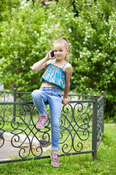 Kleines Mädchen telefoniert mit Handy gegen Grün des Parks in Summen — Stockfoto