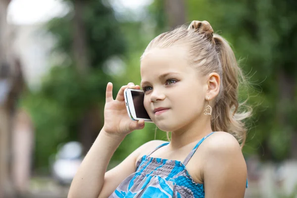 Маленька дівчинка розмовляє на мобільному телефоні проти зеленого парку в сумі — стокове фото