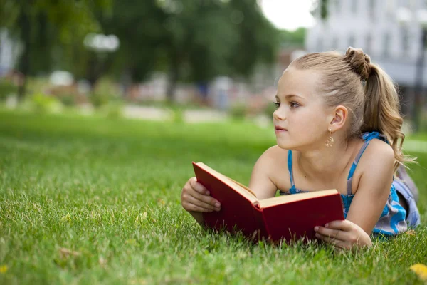 Симпатичная маленькая девочка читает книжку на улице на траве. — стоковое фото