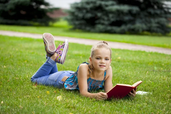 Rozkošný roztomilá holčička, čtení knihy venku na trávě — Stock fotografie