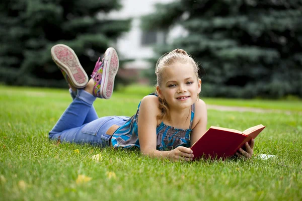 Rozkošný roztomilá holčička, čtení knihy venku na trávě — Stock fotografie
